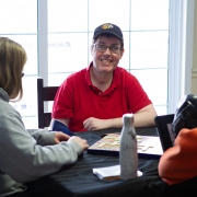 Male client smiles candidly at the camera while playing scrabble at a table with female staff.