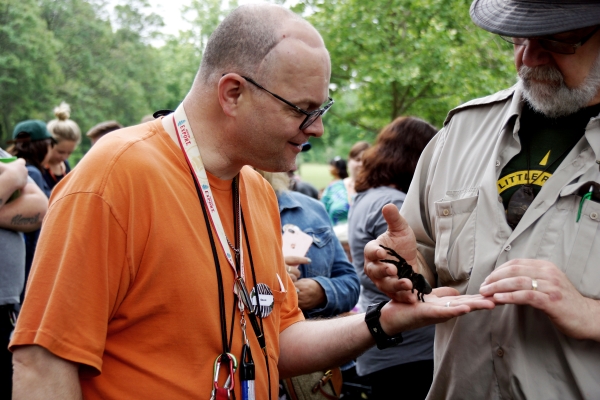 Male client looks on intently while an exotic animal exhibit staff member places a large black spider in his outstreched hand at an exotic animal exhibit at the annual client picnic.