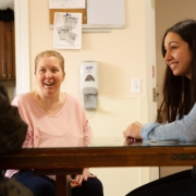 Female client smiling and sitting across the table from another client and beside female staff member. They look to be in an interesting and happy conversation.