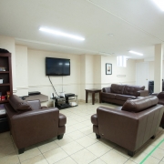 Well lit, beige basement with 3 brown leather couches and a TV and sound system