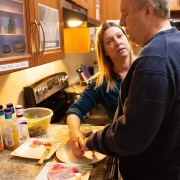 Male client and female staff are standing side by side at a kitchen counter working together preparing food.