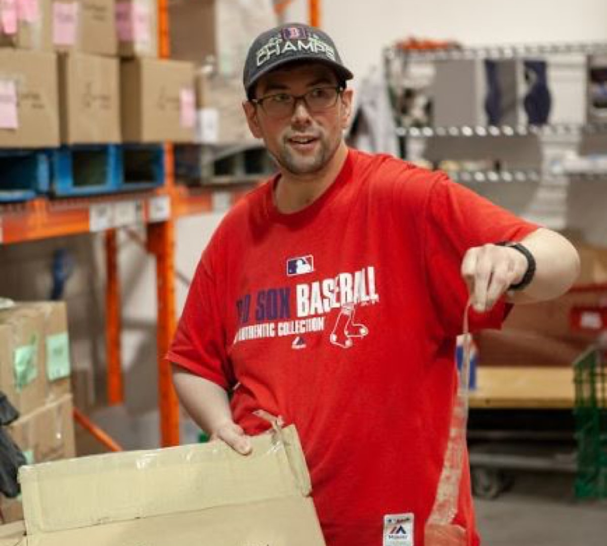 Male client is smiling while standing in a wearhouse holding a peice of cardboard while he breaks down boxes at food bank during volunteer placement.
