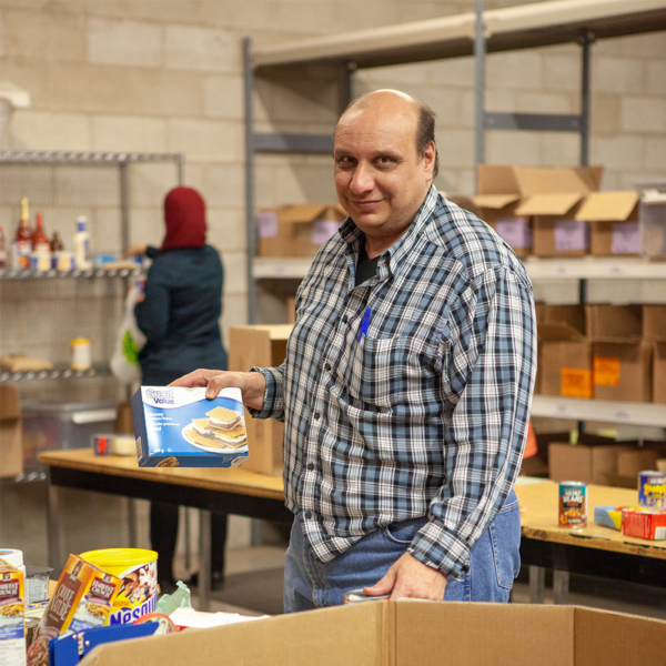 Male client organizing food donations at food bank during volunteer placement